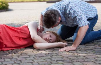 Unconscious woman lying on a pavement and a man checking her pulse